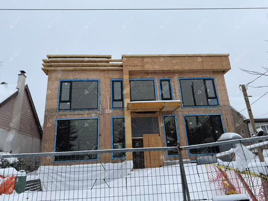 Modern house under construction with black aluminum windows and doors, surrounded by snow at a residential building site.