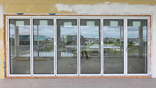 White aluminum folding door with six glass panels overlooking a residential waterfront view.